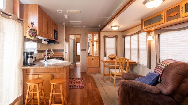Une cuisine compacte pour camping-car, équipée d’un évier, d’une cuisinière et de quelques tabourets de bar.
