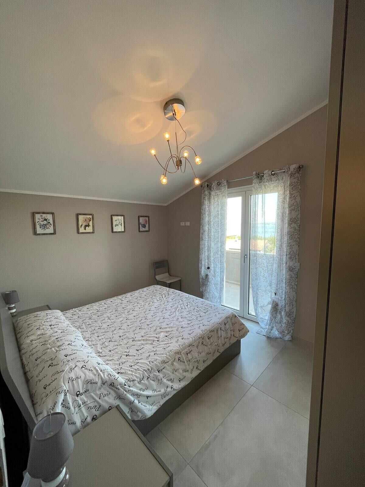 A bedroom with a bed, a chair, a bedside table, a lamp, and a ceiling light fixture.