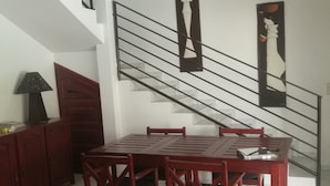 Un coin repas avec une table et des chaises en bois rouge, un escalier avec une rampe noire et un ventilateur de plafond.