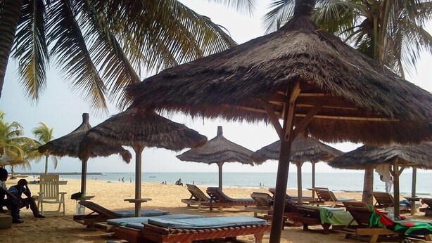 Une plage avec des parasols en chaume et des chaises longues en bois.