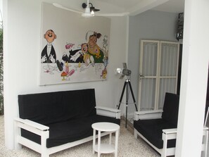 A room with a white ceiling fan, a black and white sofa, a small white table, and a tripod-mounted projector.
