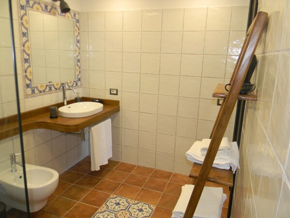 Un baño con lavamanos, espejo y bidé. Hay toallas y un estante de madera.