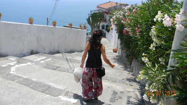 A person walking down a stone staircase with potted plants on the sides, overlooking a body of water.