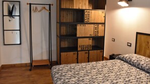 A bedroom with a bed, a wooden wardrobe, a clothing rack, and a wall-mounted mirror.