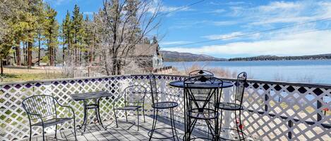 A wooden deck with outdoor seating, overlooking a lake and mountains.