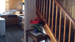 A kitchen with wooden cabinets, a dining area with a table and chairs, and a staircase with wooden railings. - Wester Riechip by Interhome (Dunkeld)