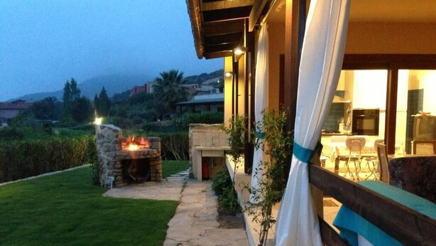 A stone pathway leading to a stone fireplace, a covered outdoor seating area, and a view of a hillside. - villa Erika 8 (Cagliari)