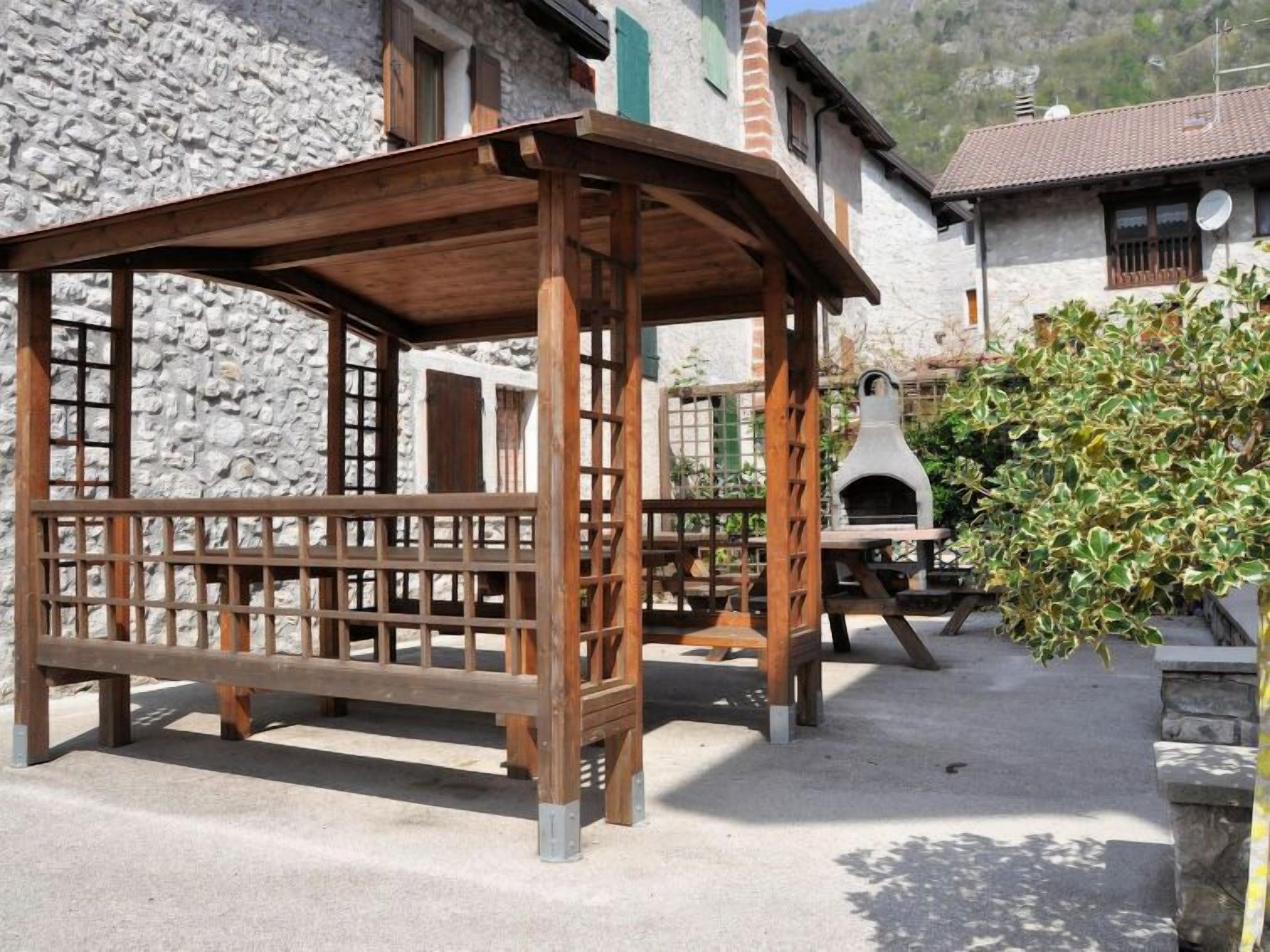 Een rustieke buitenruimte met een houten pergola, stenen muren en een traditionele stenen bakoven.