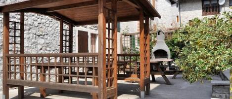 Een rustieke buitenruimte met een houten pergola, stenen muren en een traditionele stenen bakoven.