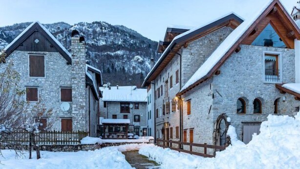 A snow-covered village with stone buildings, a wooden fence, and a stream.