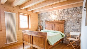 A wooden bedroom with a stone wall, a wooden bed, a radiator, and a window.