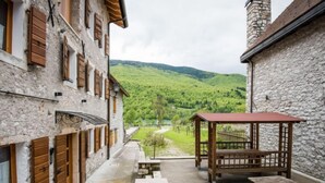 A courtyard with stone buildings, wooden shutters, a wooden pergola, and picnic tables.