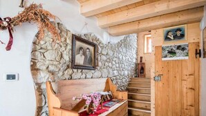 A rustic interior with a stone wall, wooden bench, staircase, and wooden door.