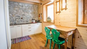 A kitchen with stone walls, wooden cabinets, a wooden table, and green chairs.