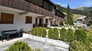 A multi-story hotel with wooden balconies, a patio area with a bench, and neatly trimmed shrubs. - Monti Pallidi by Interhome (Canazei)