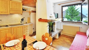 A cozy kitchen with wooden cabinets, a dining table with a checkered tablecloth, and a window with a view of greenery outside. - Monti Pallidi by Interhome (Canazei)