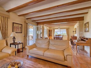 A spacious living room with a beige sofa, a dining table, and a wooden ceiling.