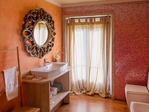 Un baño con tocador de madera, espejo, lavamanos, inodoro y cortina de ducha.