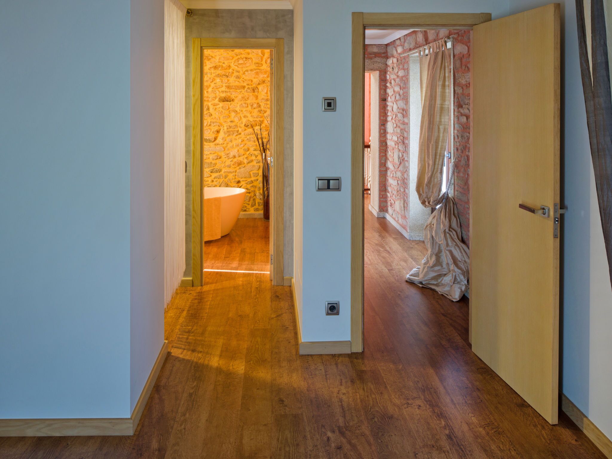 A hallway leading to a bathroom with a stone wall and a bathtub.