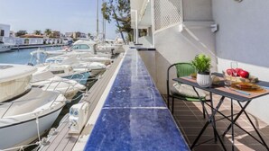 A balcony with a view of a marina, a table with a plant and fruit, and a chair. - Apartment Symar by Interhome (Roses)
