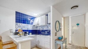 A compact kitchen with white cabinets, a blue-tiled backsplash, and a wooden dining table. - Apartment Symar by Interhome (Roses)