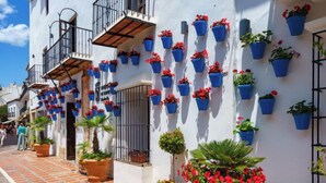 A white building with blue hanging flower pots and potted plants on the ground. - Mirador II by Interhome (Marbella)