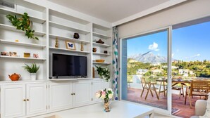 A modern living room with a flat-screen TV, white cabinets, and a balcony with a mountain view. - Mirador II by Interhome (Marbella)