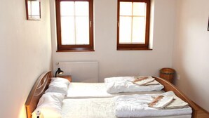 A bedroom with two beds, a bedside table with a lamp, a radiator, and two windows.