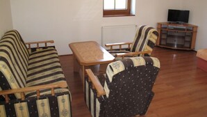 A living room with a sofa, armchairs, a small table, and a TV stand.