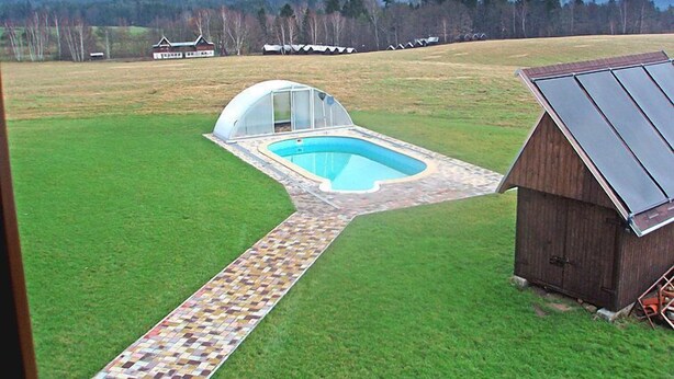 A swimming pool with a glass enclosure, a wooden shed, and a clear view of mountains in the background.