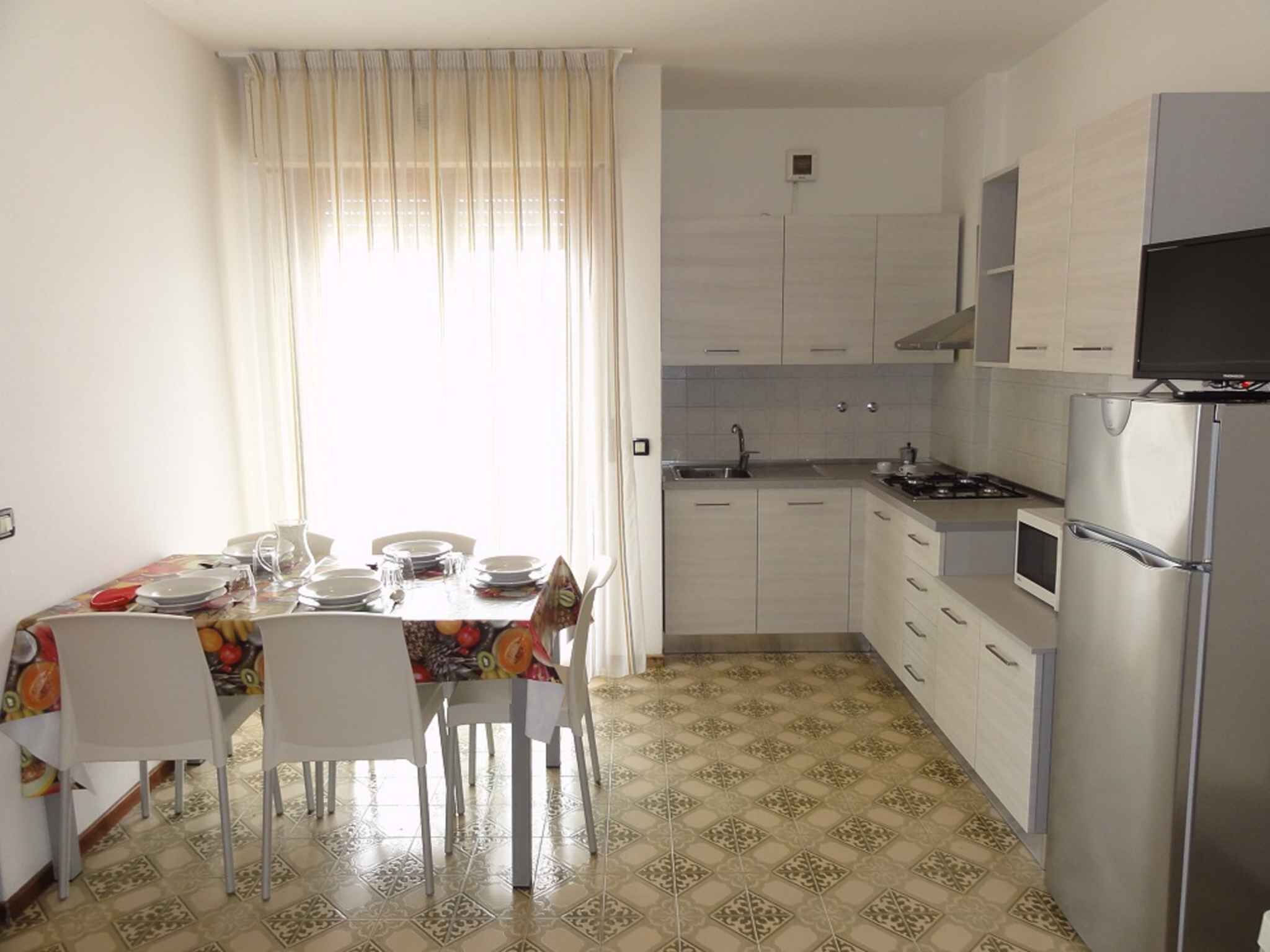 Une cuisine compacte avec des meubles blancs, un réfrigérateur en acier inoxydable et un coin repas avec une table dressée pour quatre personnes.