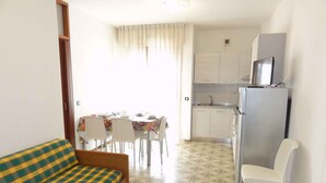 A compact living space with a sofa, dining table, chairs, a kitchenette, and a TV. - Holiday apartment on the beach (Bibione)