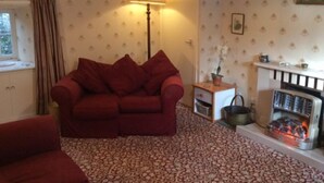 Una sala de estar acogedora con un sofá rojo, alfombra estampada, chimenea y una lámpara.