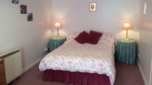 Un dormitorio con colcha estampada, dos lámparas de noche y un radiador.