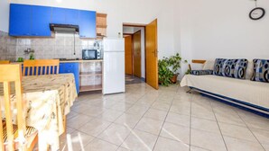 Een compact appartement met kitchenette, eethoek en woonkamer met een bank en wandlamp.