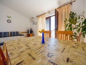 Un comedor con una mesa cubierta con mantel de motivos de café, un jarrón azul con flores amarillas y una planta a la derecha.