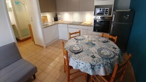 Una cocina compacta con armarios blancos, una mesa de comedor con mantel estampado y un horno empotrado.