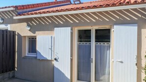 Un edificio de una sola planta con techo de tejas, puerta corredera de vidrio y una ventana pequeña con contraventanas.