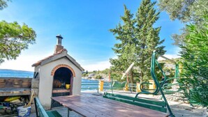 Un espace extérieur aménagé près de la plage, avec un banc en pierre, une table de pique-nique et une petite construction en briques dotée d’une cheminée.