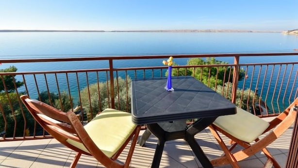 Un balcon avec une table et deux chaises, donnant sur une mer calme et une terre lointaine.