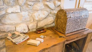 Une table en bois, avec un mur en pierre en arrière-plan, une malle en bois et divers objets, notamment des livres et une petite boîte.