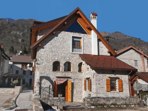 A stone building with a sloped roof and wooden beams, featuring a small balcony and a chimney.