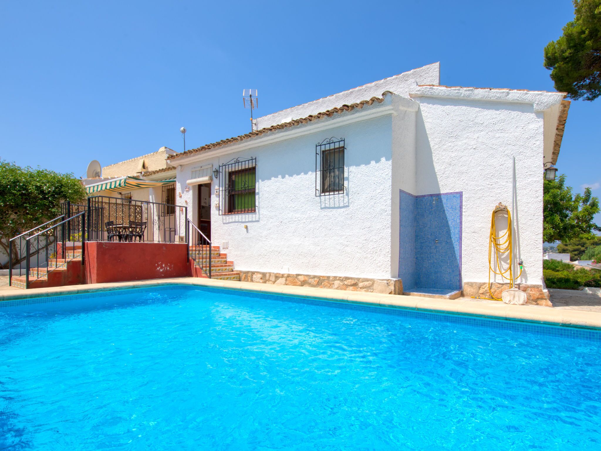 A white building with a pool, a red staircase, and a blue tiled wall.