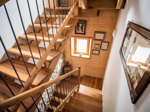 Una escalera de madera con base de pared de piedra, un tragaluz pequeño y cuadros enmarcados en las paredes.