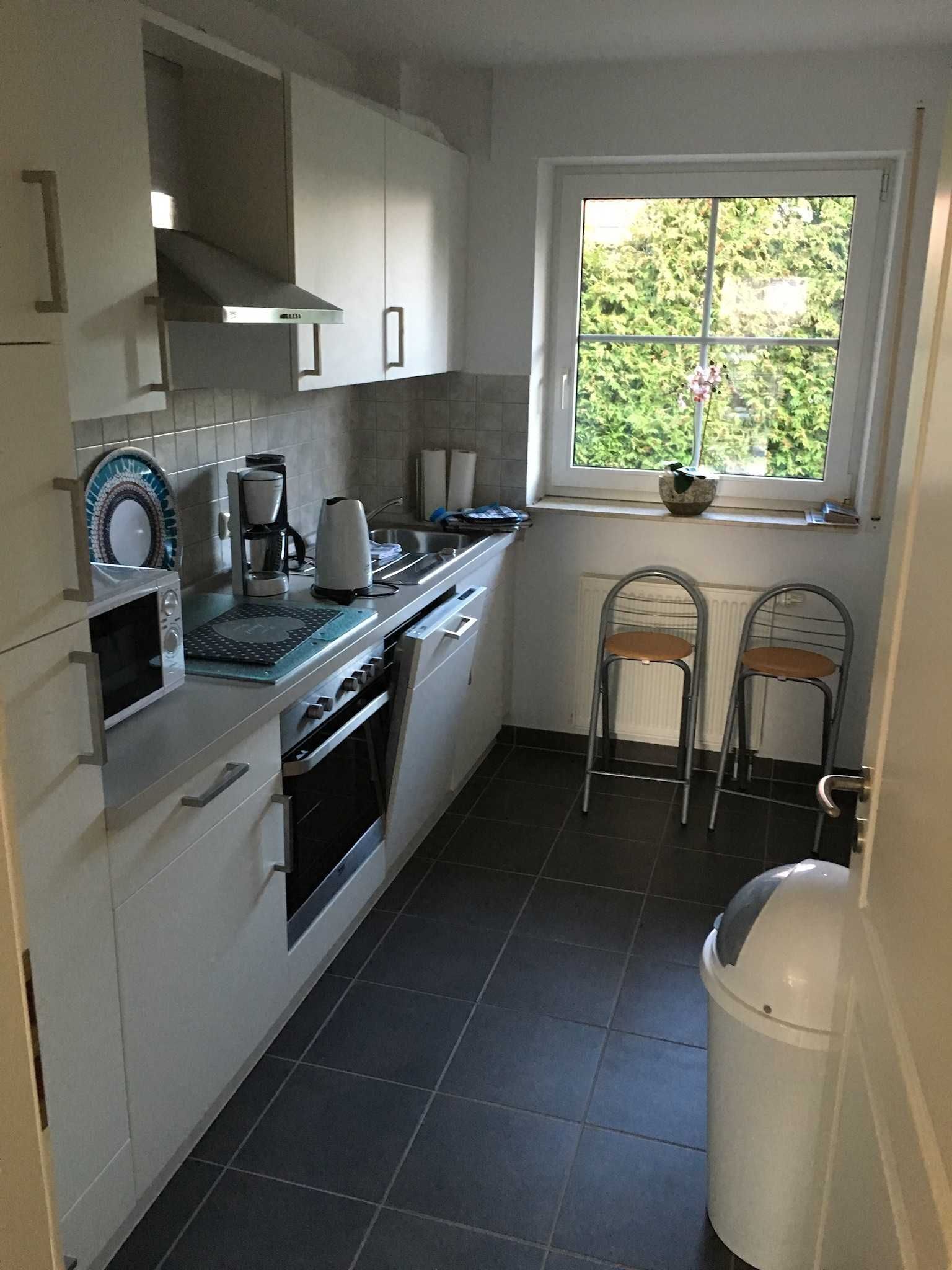 A compact kitchen with white cabinets, a stove, a sink, and a window with a view of greenery.