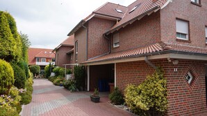 Een woongebouw met een bakstenen gevel, een overdekte oprit en een kleine tuin met verschillende planten.