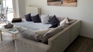 Een woonkamer met een bank, kussens, een klein tafeltje met een mand en een lijst met een foto aan de muur.