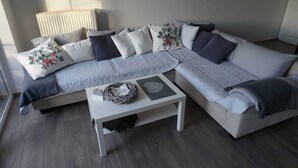 Een moderne woonkamer met een hoekbank, een witte bijzettafeltje en een rieten mand.