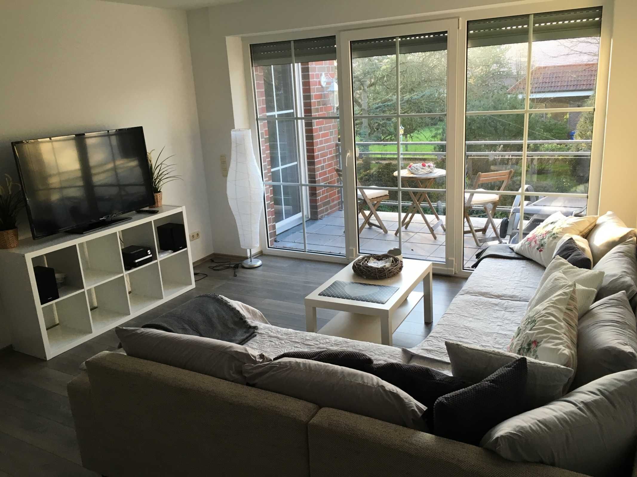 Una sala moderna con sofá, televisor y vistas a un balcón con mobiliario exterior.