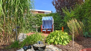 A garden with a pond, rocks, and a blue and white striped chair. - Holiday house North Sea snail (Esens)